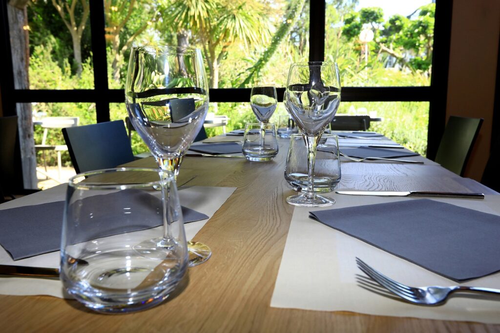 A nice table set in a room restaurant. outside, can we sea a luxurious garden